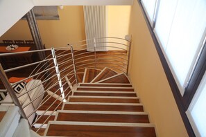 Un escalier en colimaçon avec des rampes en métal et des marches en bois, menant à une pièce où se trouvent une table à manger et des chaises.