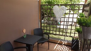 Uma pequena área de pátio com uma mesa e duas cadeiras, um objeto decorativo em formato de coração e um vaso com planta.