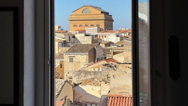 A view through a doorway of a building with a large arched window and a tiled roof. - Historic center, 2 rooms, 2 toilets, sky terrace, lift, free high speed Wi Fi (PALERMO)
