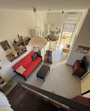 A spacious living area with a red sofa, a colorful chair, a black coffee table, a bookshelf, and a kitchen in the background. - Historic center, 2 rooms, 2 toilets, sky terrace, lift, free high speed Wi Fi (PALERMO)