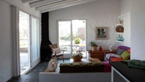 Un salón amplio con un gran ventanal corredera que da a un espacio exterior, una zona de estar acogedora con un sofá y sillones, y una chimenea.