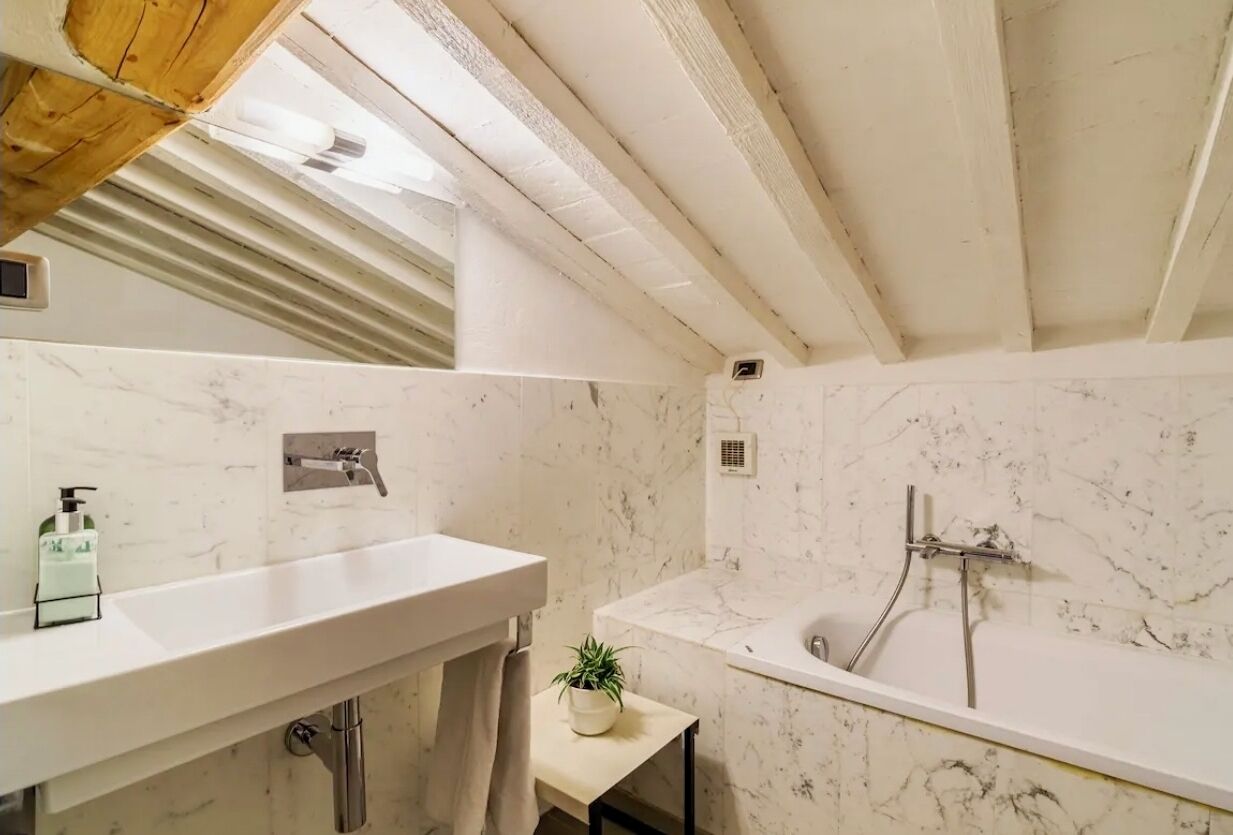 Un baño con lavamanos de mármol blanco, bañera y tragaluz.
