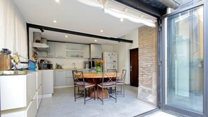 Une cuisine moderne avec un coin repas, comprenant une grande table et des chaises en bois, des meubles blancs et une porte-fenêtre coulissante donnant sur un espace extérieur.