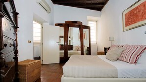 Une chambre à coucher avec un grand lit, une armoire en bois, un miroir, un panier en osier et un tableau accroché au mur.