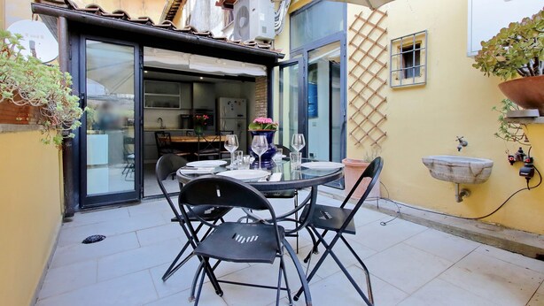 Un espace extérieur aménagé pour les repas, avec une table ronde, des chaises noires et un grand parasol.