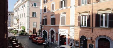 Una calle adoquinada flanqueada por edificios tradicionales, un café con mesas al aire libre y un automóvil estacionado frente a un edificio con cajero automático.