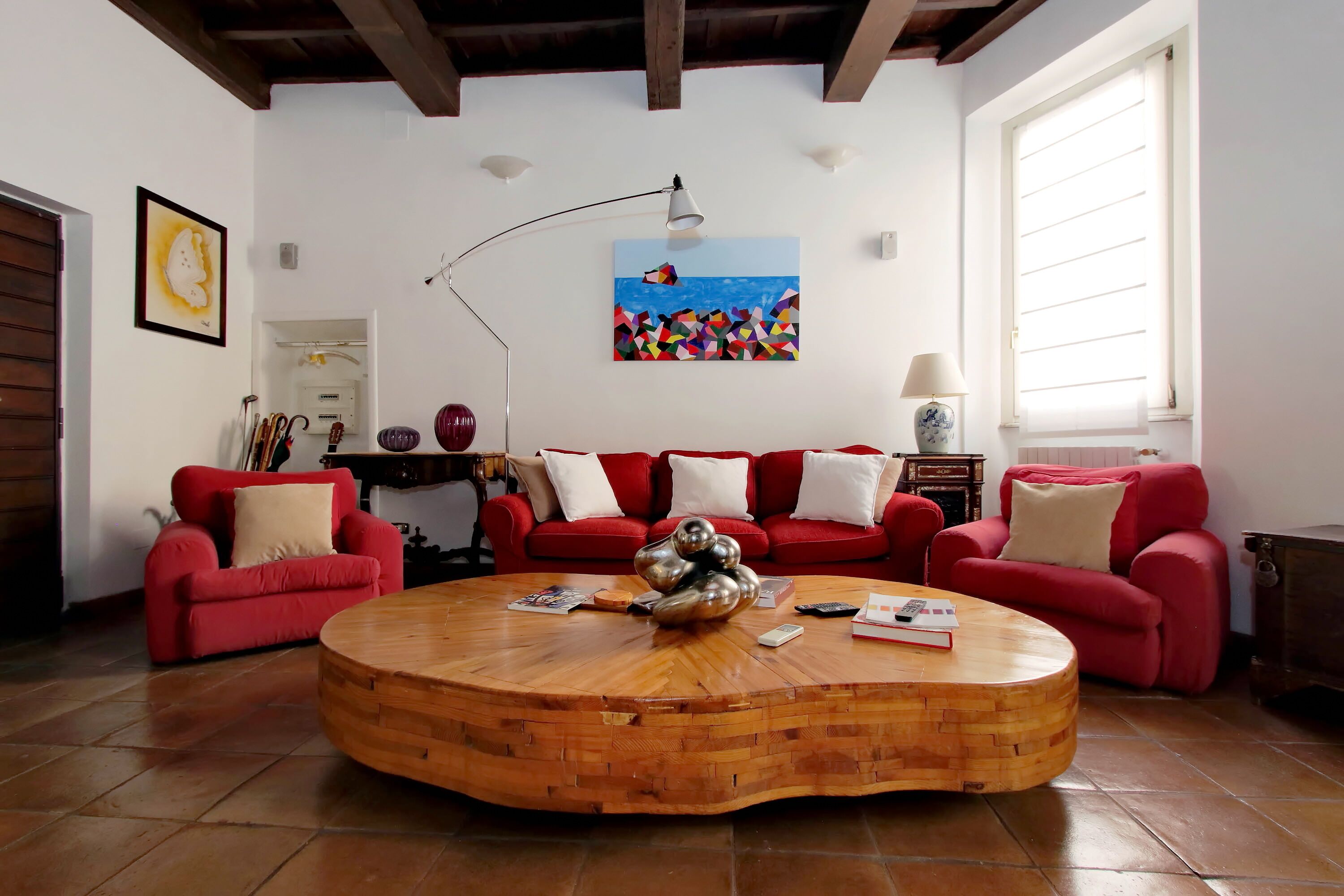 A living room with a wooden coffee table, red sofas, a painting, and a lamp.