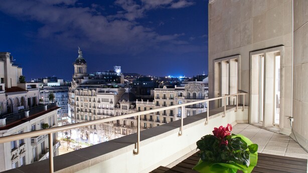Un balcon offrant une vue sur le paysage urbain nocturne, avec notamment un bâtiment imposant doté d’un dôme et d’une tour horloge.