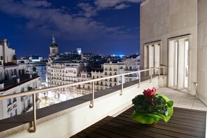 Ein Balkon mit Blick auf eine nächtliche Stadtansicht, darunter ein markantes Gebäude mit Kuppel und Uhrturm.