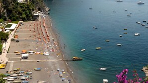A beach with numerous boats, a pier, and a rocky cliff.