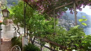 A garden with a pergola, a statue, and a view of a coastal town.