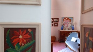 A room with a painting of a red flower, a blue sofa, a dresser with a pop art portrait, and a pink tiled floor.