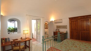 A bedroom with a bed, a desk with a chair, a window with a view, and a door leading to a bathroom. - Casa Maria 6+2, Emma Villas (Positano)