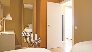 A hotel room with a bed, a desk with a lamp, a striped chair, a wardrobe, and a door leading to another room. - Property with parking, Ac,wifi, metro & at only 8 min.from city centre by metro. (Barcelona)