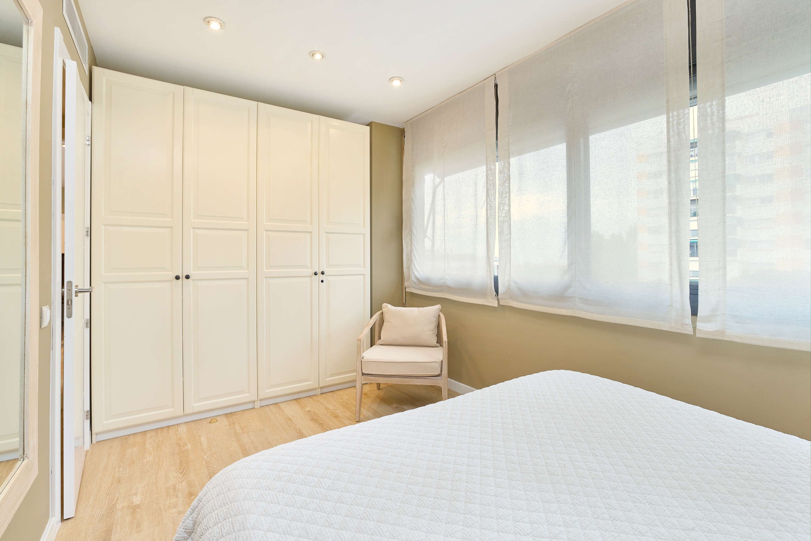 Een slaapkamer met een bed, een stoel, een kledingkast en een raam met gordijnen.