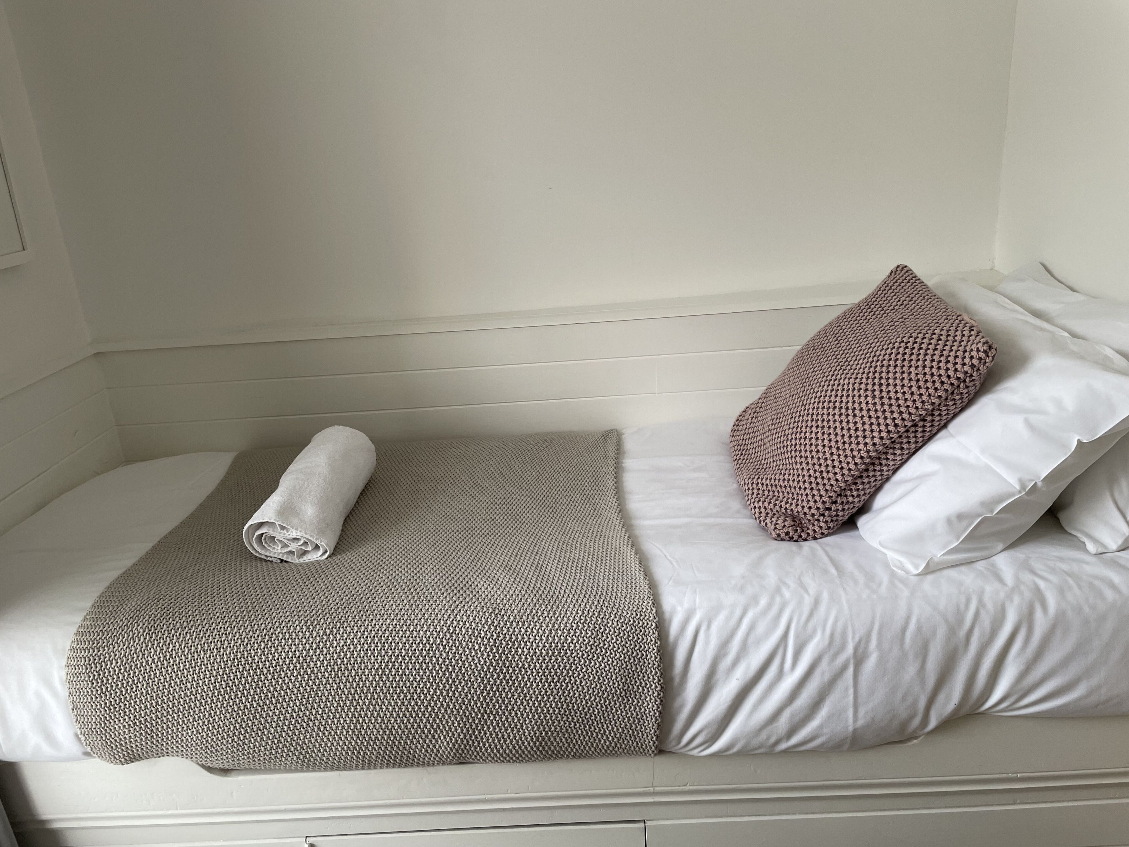 A bed with a rolled towel, a patterned blanket, and two pillows.