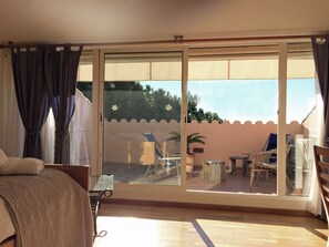 Une chambre avec un lit, une porte vitrée donnant sur un espace extérieur aménagé avec des chaises longues et une table.