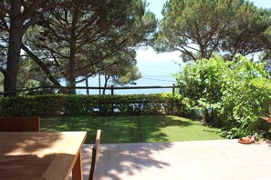 A patio with a wooden table and chairs, a well-maintained lawn, and a view of the sea. - Large luxury home, stunning views, in green oasis, private garden, huge pool (Sant Feliu de Guixols)