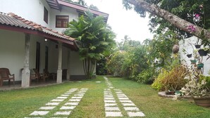A house with a tiled roof, a covered porch with chairs, and a garden with a paved walkway. - Villa Happy Home (Bentota)