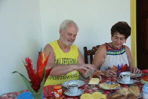 Two people seated at a table with a floral tablecloth, plates of food, and a glass of orange juice. - Villa Happy Home (Bentota)