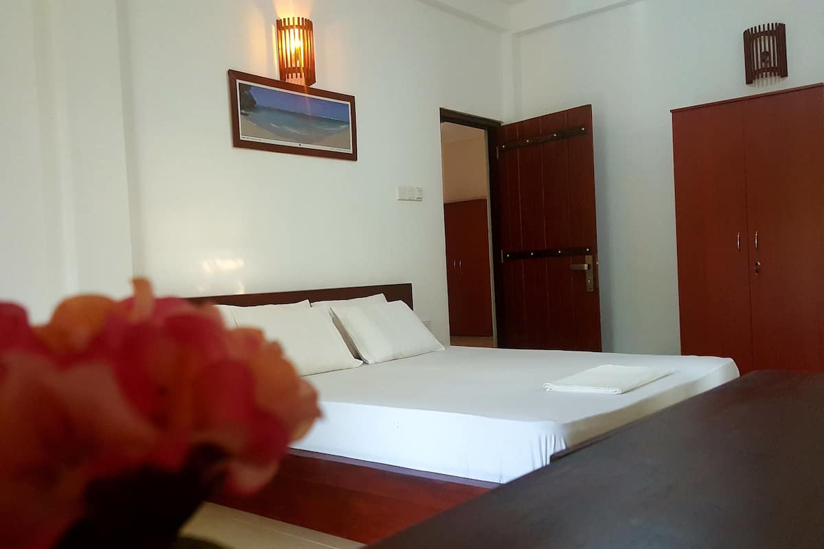 A hotel room with a bed, a nightstand, a wooden wardrobe, and a framed picture on the wall.