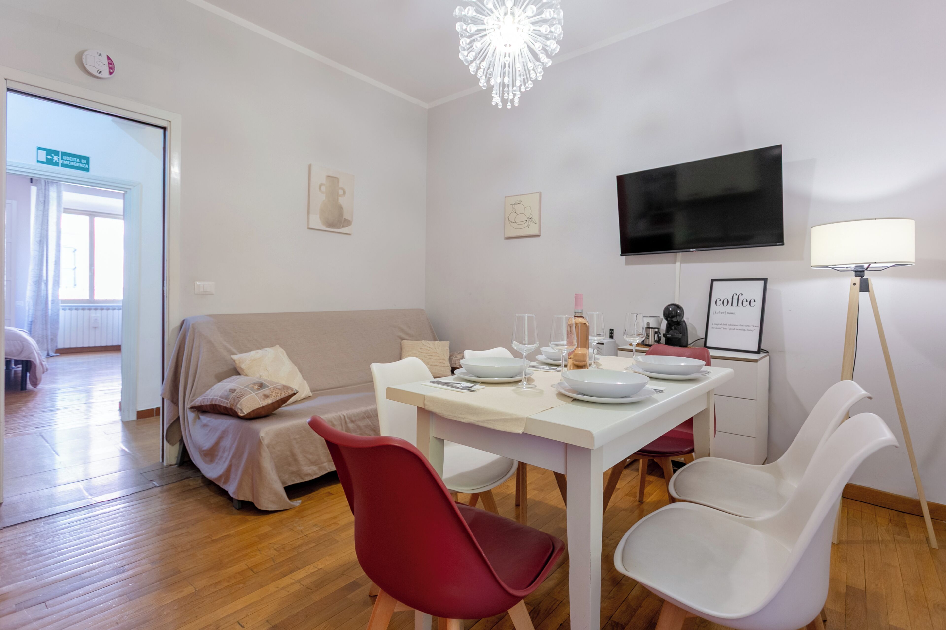 A modern living room with a dining table, red and white chairs, a television, and a chandelier.