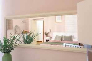A bedroom with a bed, bedside table, lamp, and a mirror reflecting the room.