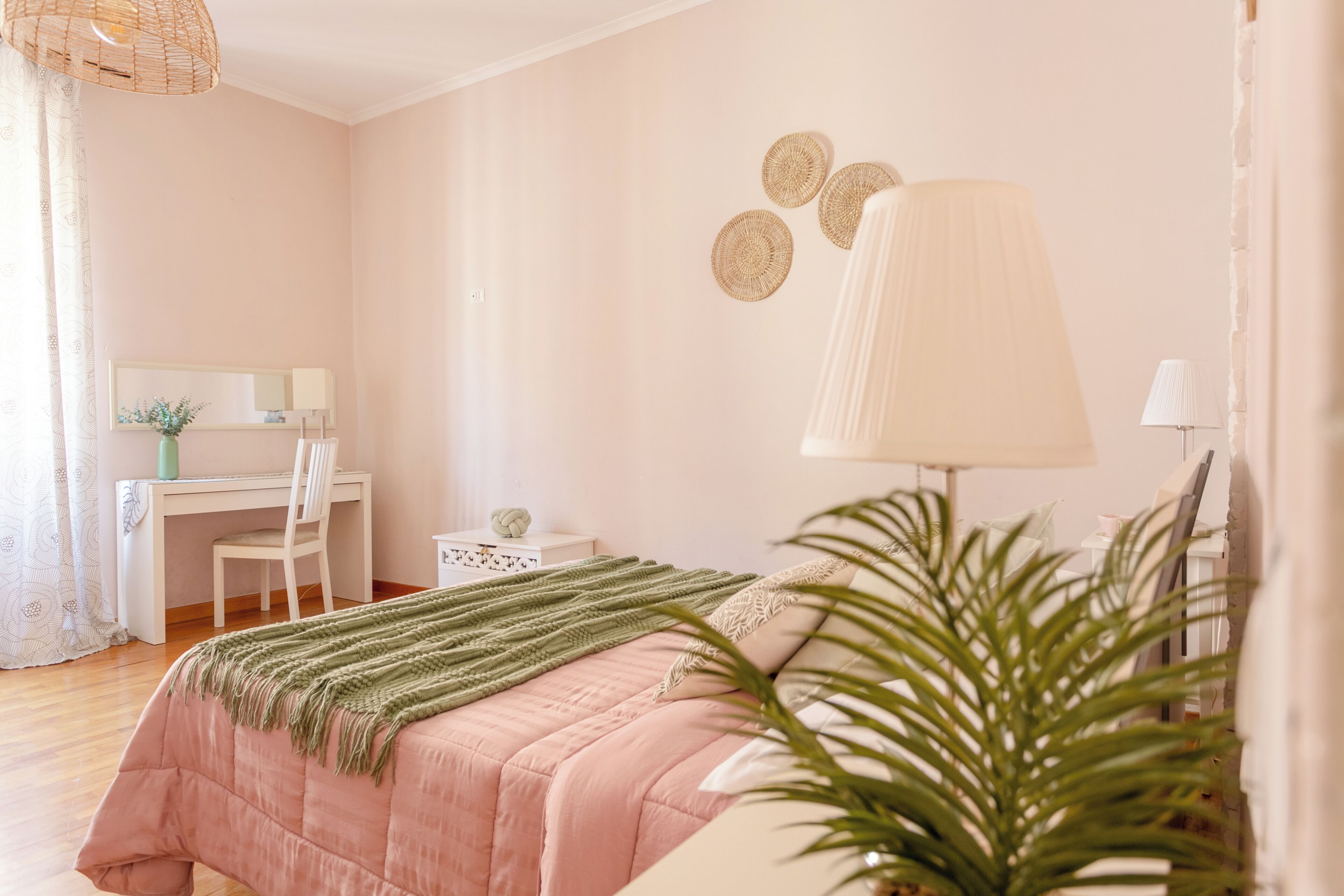 A bedroom with a bed, desk, chair, lamp, and a plant.