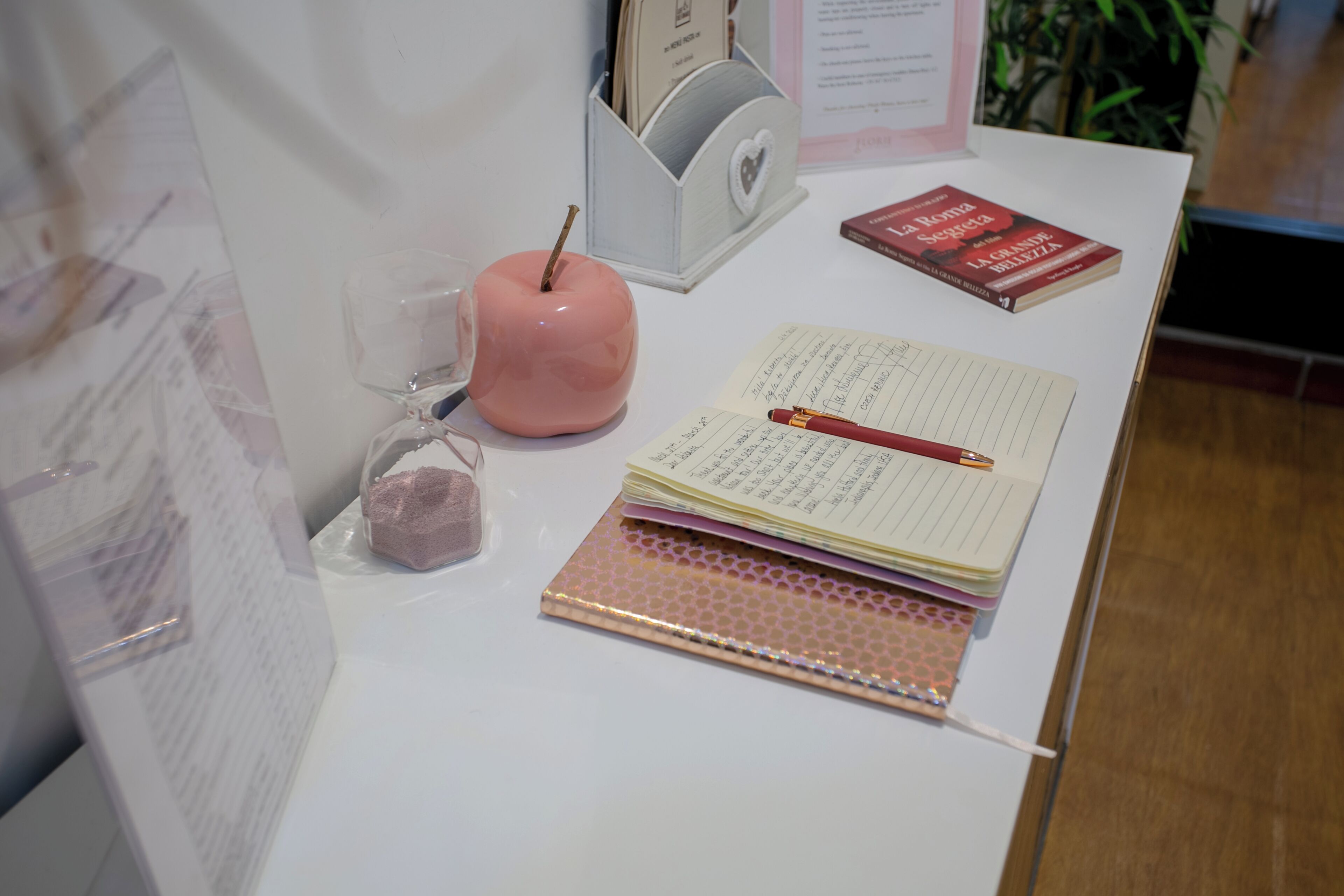 A desk with a pink apple, a notepad, a pen, and a book.