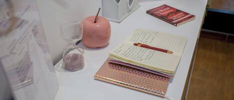 A desk with a pink apple, a notepad, a pen, and a book.