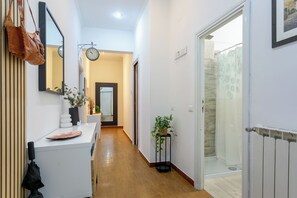 A hallway with a white counter, a hanging brown bag, a potted plant, and a door leading to a shower area.