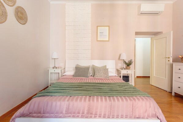 A bedroom with a bed, nightstands, a wall-mounted air conditioner, and a framed picture.