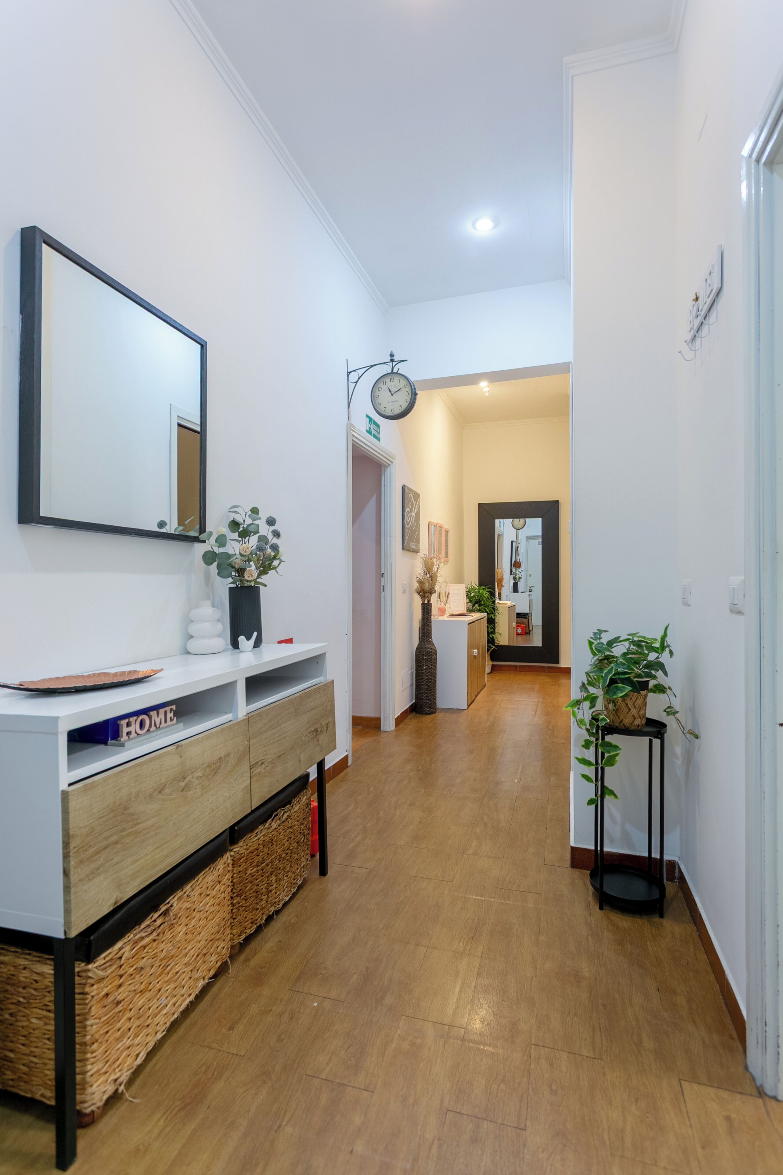 A hallway with a white console table, a clock, and a potted plant.