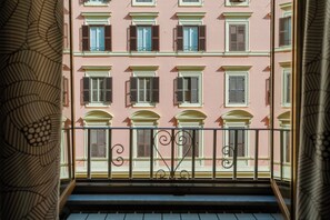 A balcony with a wrought iron railing, overlooking a row of pink buildings with multiple windows and shutters.