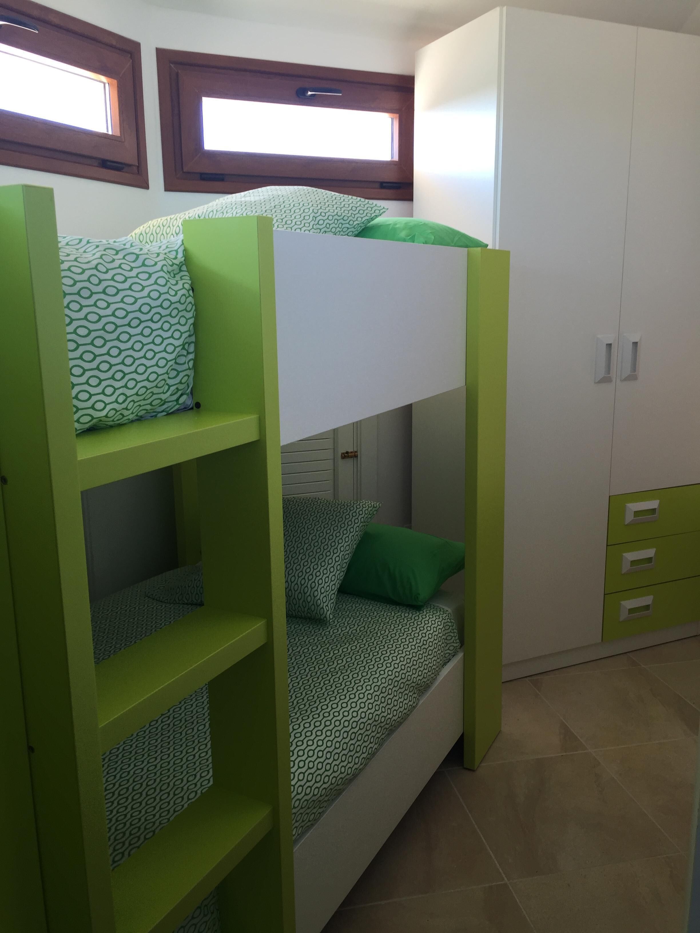Una cama litera con ropa de cama verde y blanca, un armario blanco y una ventana con persianas.