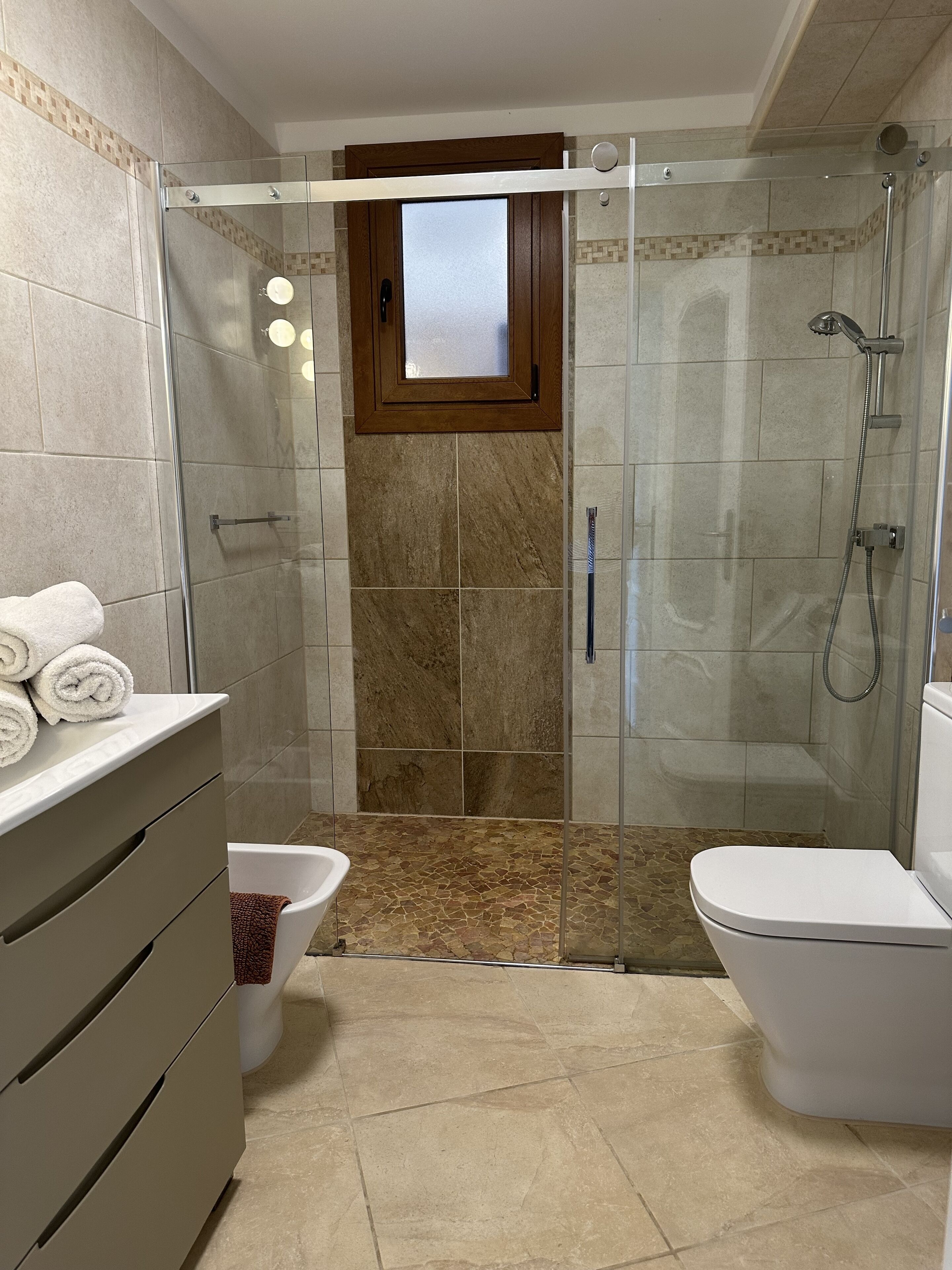 A modern bathroom with a glass-enclosed shower, a toilet, and a sink with a towel rack.