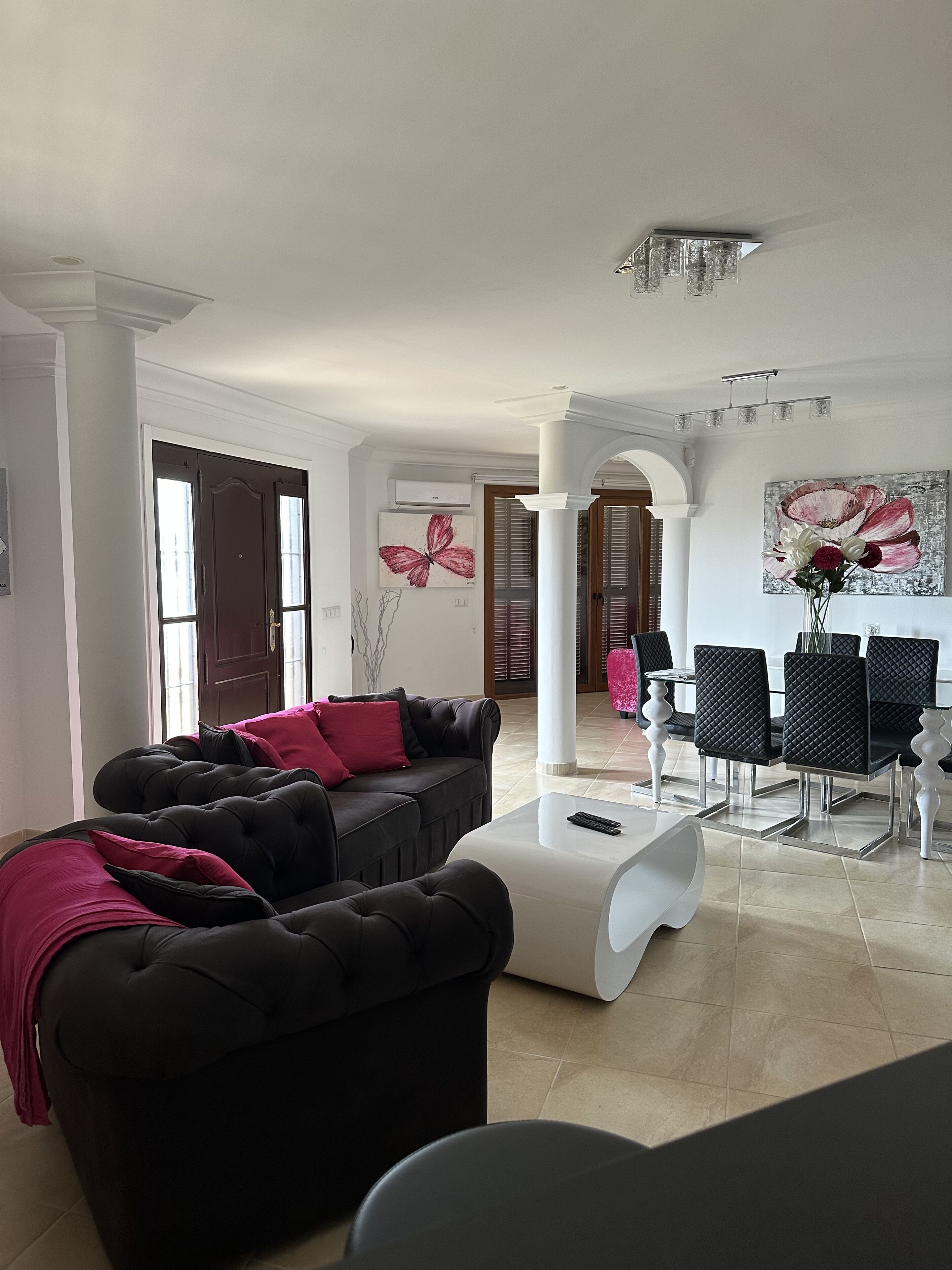 A modern living room with a black sofa set, a white coffee table, and a dining area with black chairs and a white table.