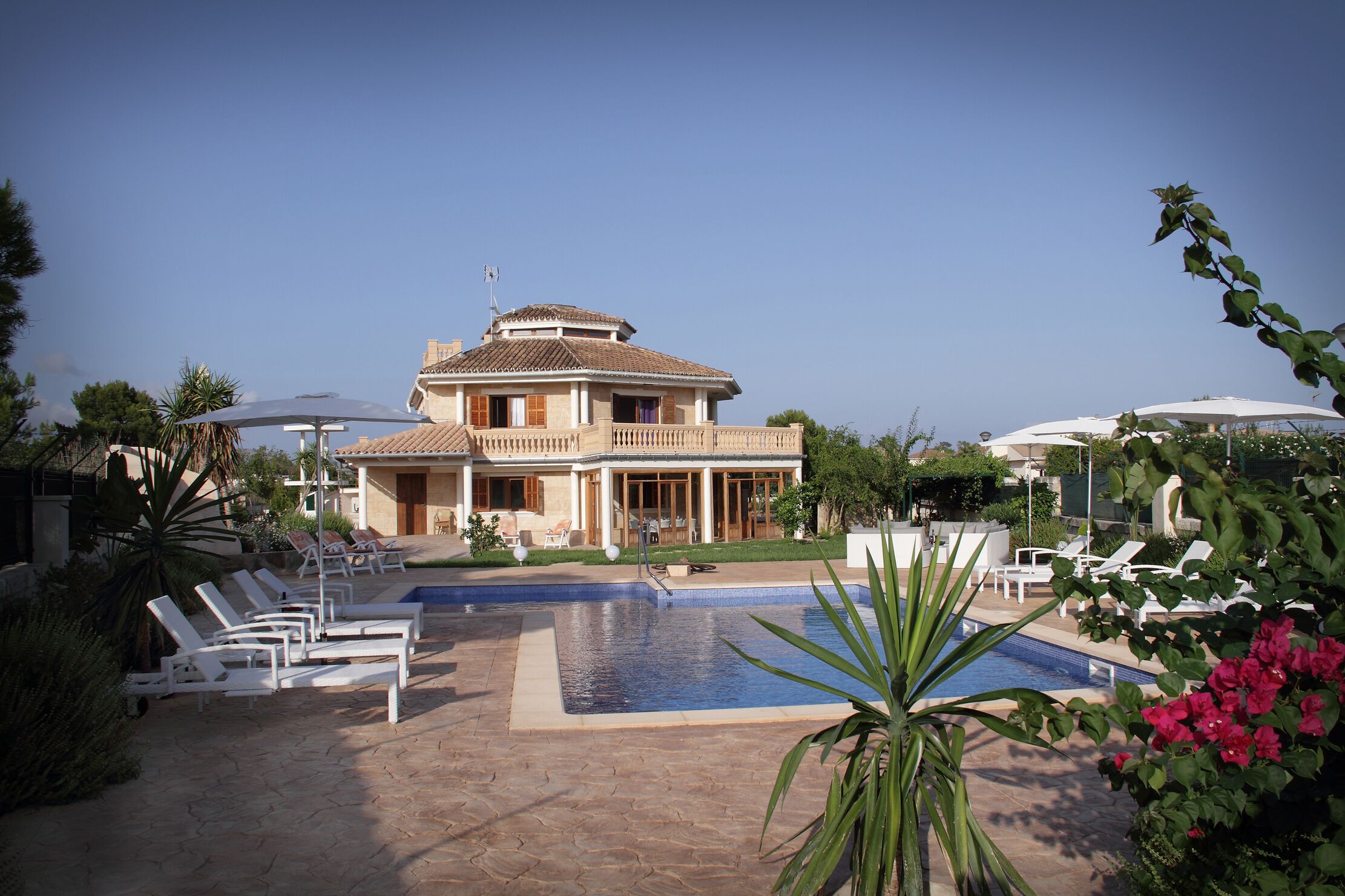 Une grande maison avec une piscine, des chaises longues et des parasols.
