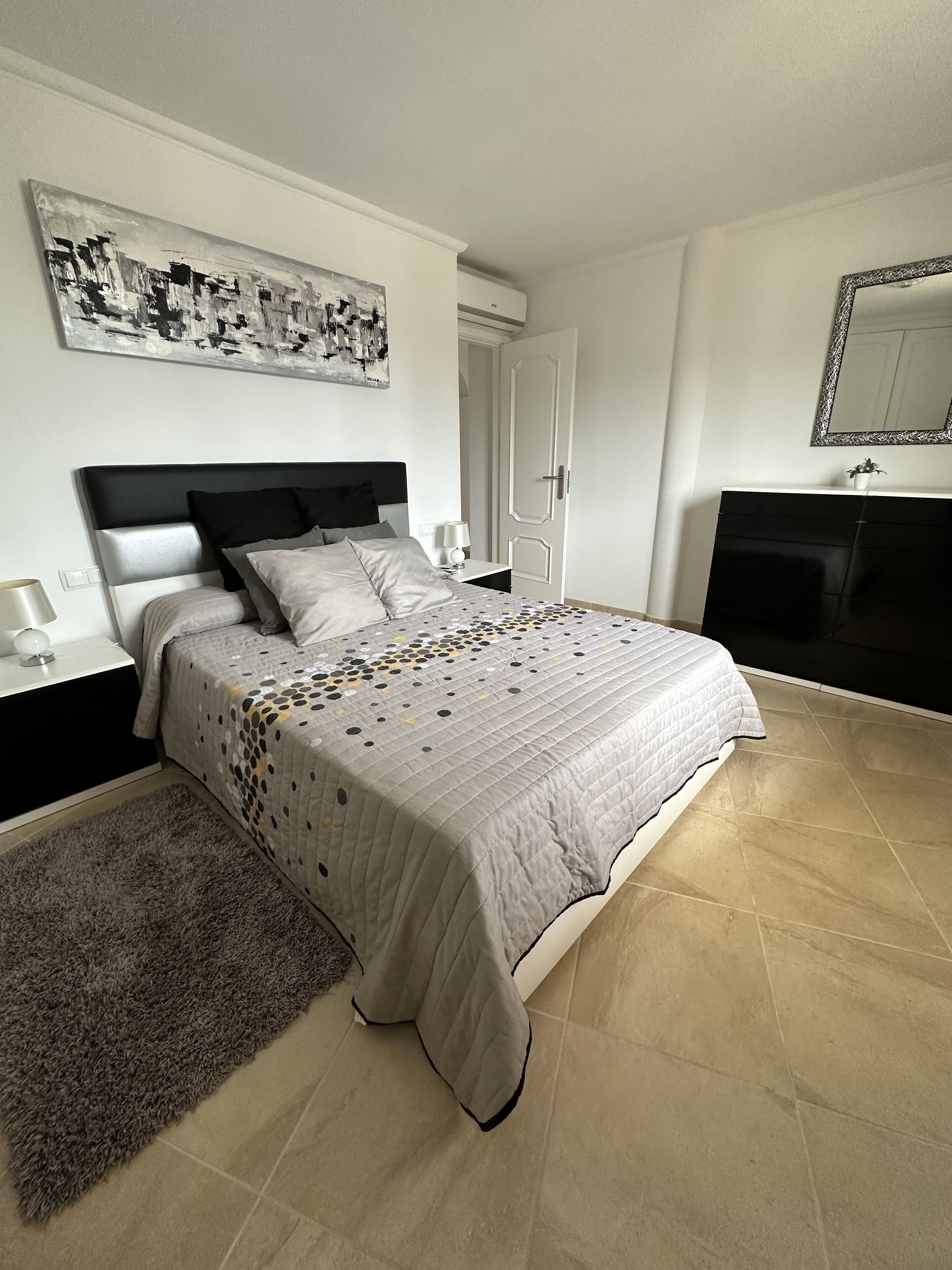 Un dormitorio con cama, mesitas de noche, un espejo y un cuadro en la pared.