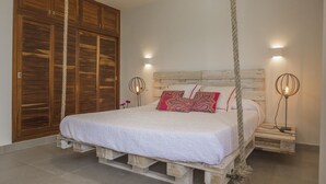 A bedroom with a bed on a wooden pallet base, a wooden wardrobe, and two wall-mounted light fixtures.