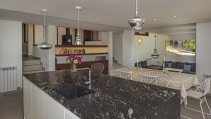 A modern kitchen with a marble island, pendant lights, and a dining area with white chairs.