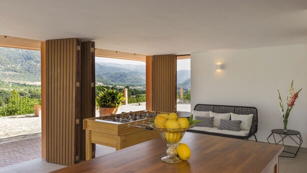 A modern room with a wooden table, a foosball table, a sofa, and a view of mountains.
