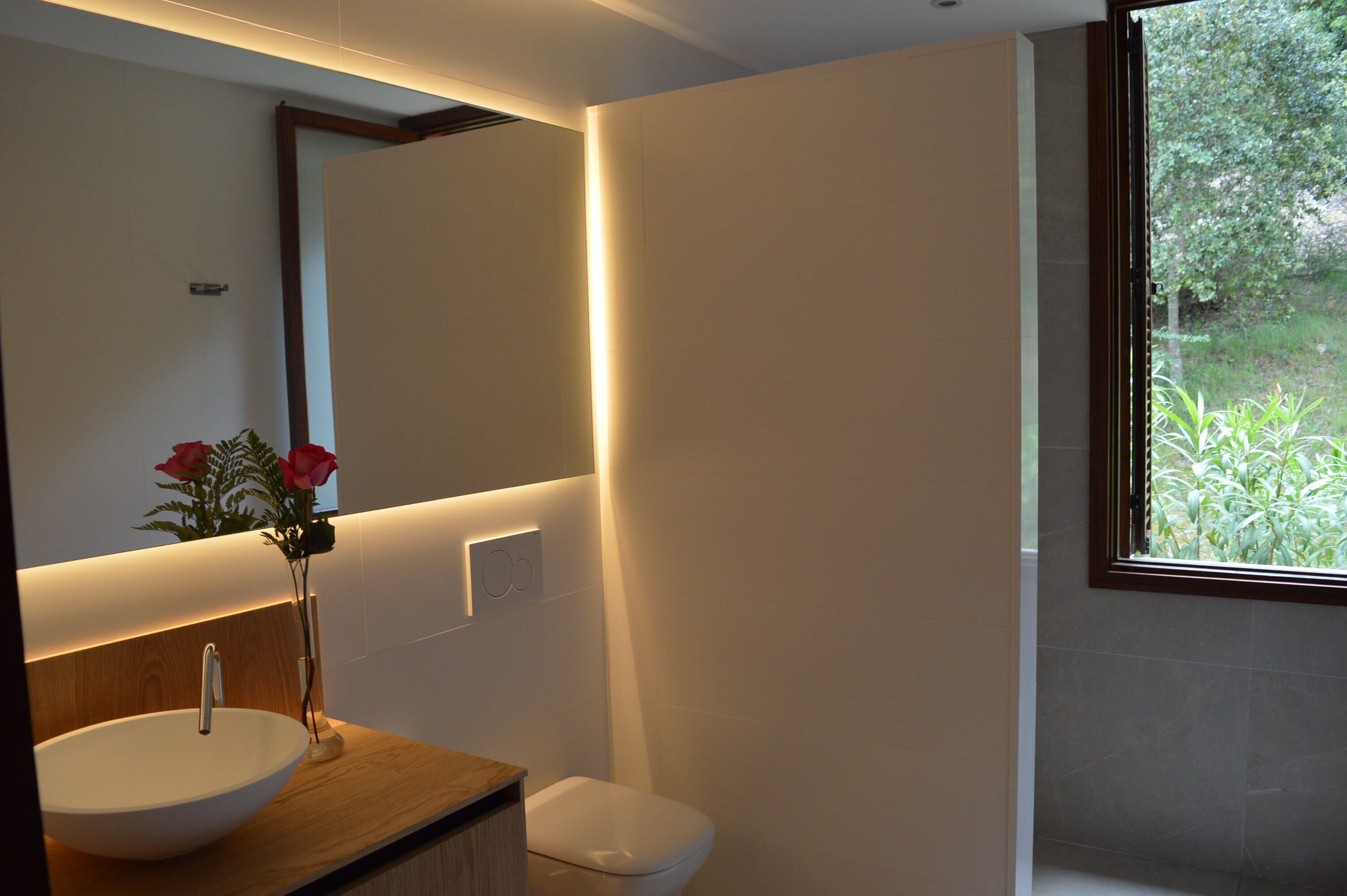 A modern bathroom with a wooden vanity, a white sink, and a large mirror.