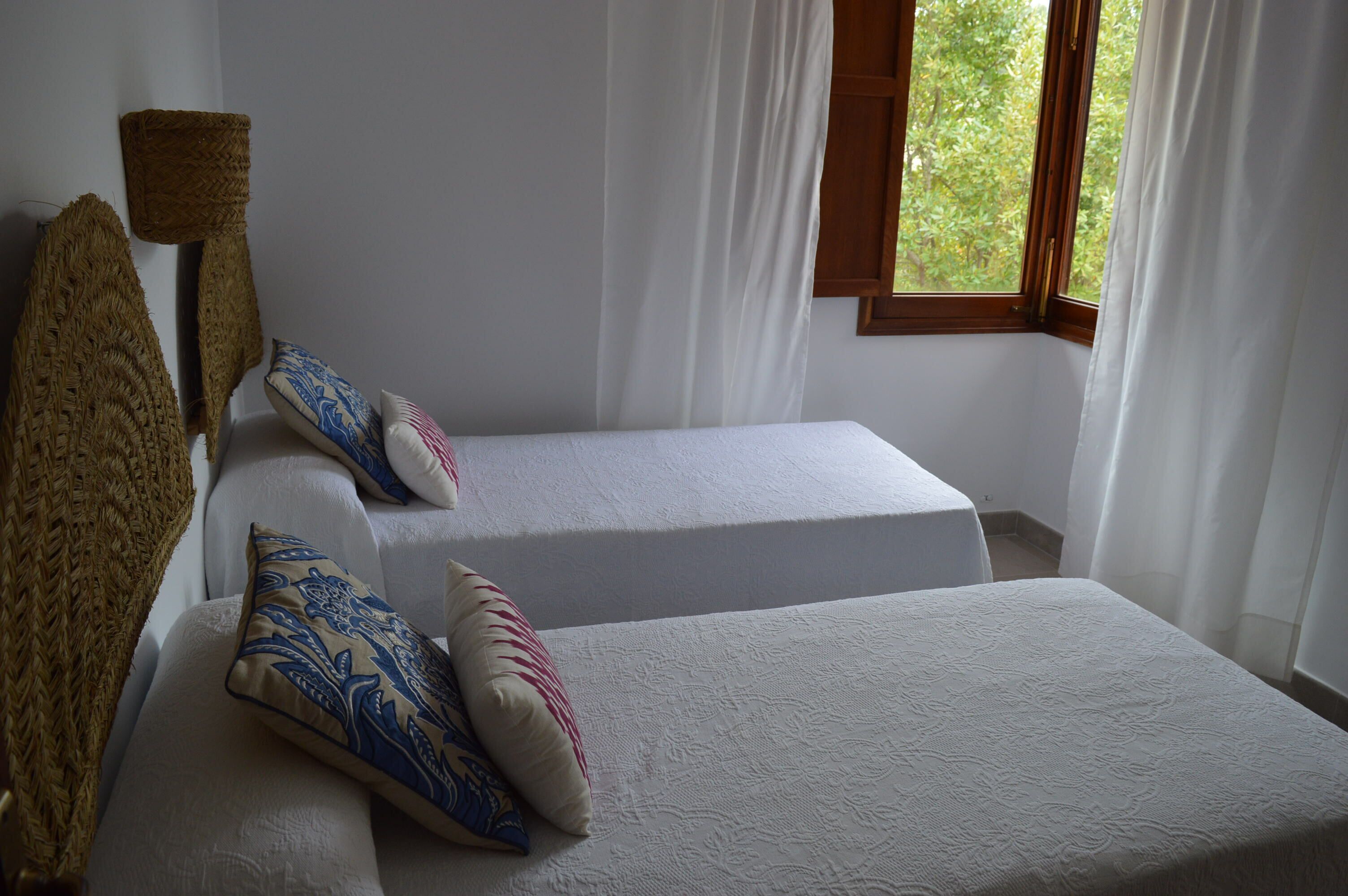 Ein Zimmer mit zwei Einzelbetten, weißer Bettwäsche und einem Fenster mit Vorhängen.