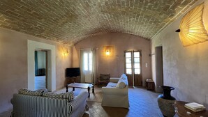 A cozy living room with a brick ceiling, a striped sofa, a white armchair, a wooden coffee table, and a large vase on a wooden side table. - Pigna: Charming village house, 5 km from the sea, vaulted and whitewashed (Pigna)