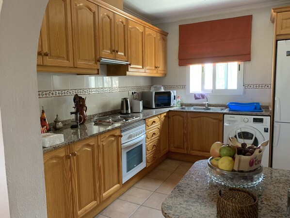 Une cuisine avec des meubles de rangement en bois, un four à micro-ondes, un grille-pain, un évier et un lave-linge.