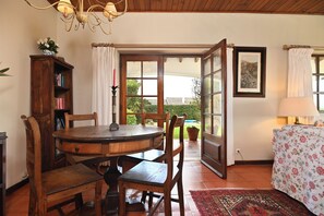 A room with a wooden dining table, chairs, a bookshelf, a window with curtains, and a door leading outside. - Casa do Moinho, villa with a heated pool near the beach in Sintra, self check-in (Ulgueira-Colares)