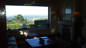 Una habitación con un amplio ventanal que ofrece vistas a un paisaje, una chimenea y una mesa con objetos encima.