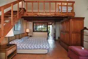 A bedroom with a wooden staircase, a bed with a floral bedspread, a nightstand, a wardrobe, and a view through a window.