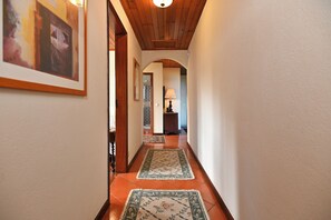 A hallway with wooden ceiling, tiled floor, and framed artwork on the walls.